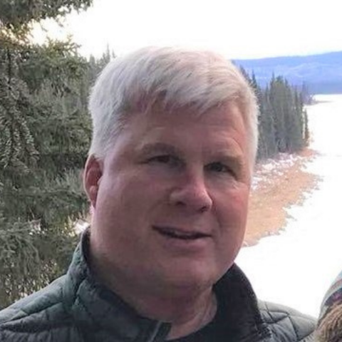 man with white hair stands near a snowy lake