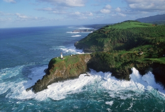 A lighthouse sits on a peninsula. Waves crash around the area.
