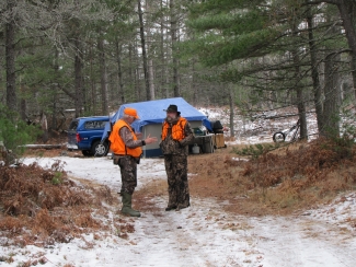 Two men wearing blaze orange in front of a hunting camp.