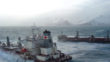 The M/V Selendang Ayu split in two, with each half aground in heavy surf. Waves wash over the deck of the stern portion.