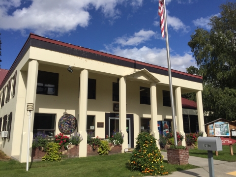 A historic two story building from the 1930's with six columns, painted tan with a brown trim and red roof. 