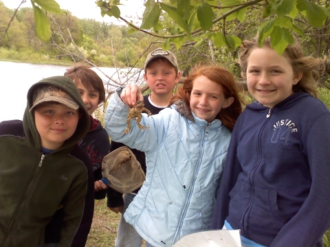 Students gathered around with the one in the middle holding a frog.