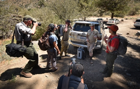 Multiple people with photography equipment stand outside in a group