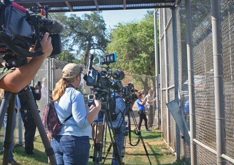 Multiple people with video cameras stand outside a large fenced area