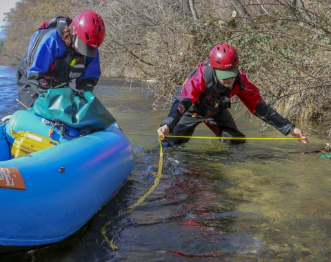 two people standing in a river people bending down measuring something.