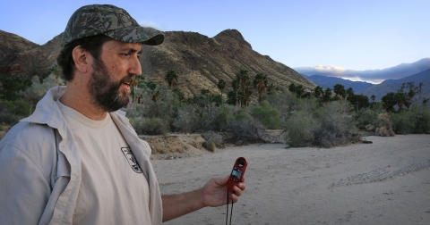 Standing man holds small electronic device in left hand