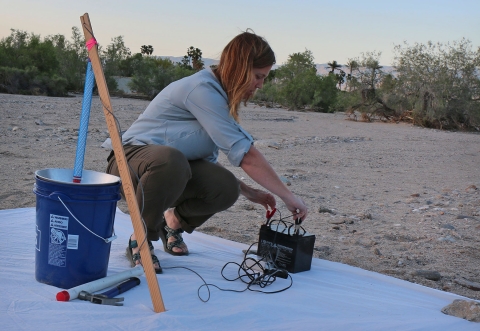 Woman squatted down on tarp works on equipment