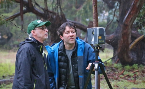 Two standing men look at equipment on tripod