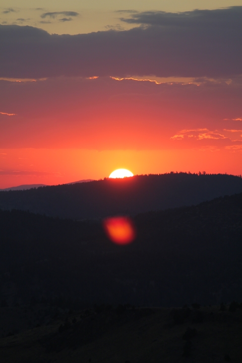 Sun setting over the hill in sagebrush country. The sky is a bright reddish-orange.