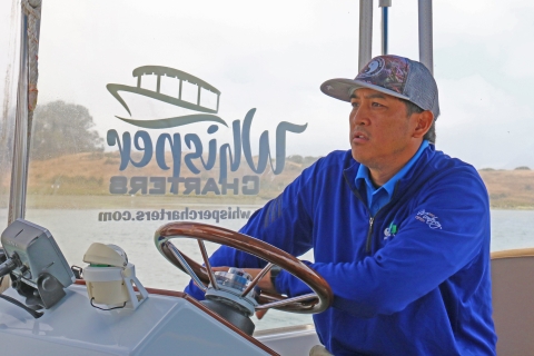 A man wearing a blue jacket driving a boat