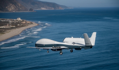 A white aircraft flies over the ocean