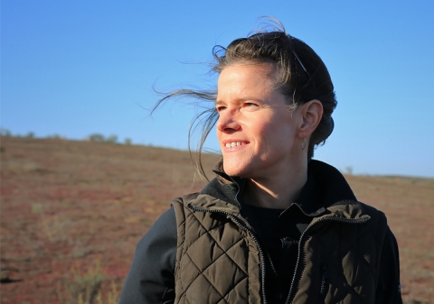 Woman looks across grassland landscape over her right shoulder.