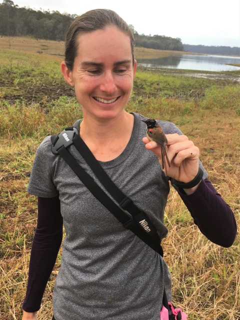 A woman holds a small bird in her fingers.