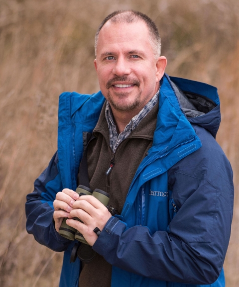 A man in a blue all-weather jacket holding a pair of binoculars