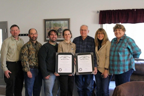 seven people stating in a row. two in center hold awards