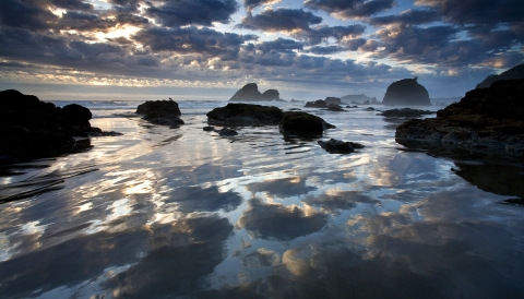 a cloudy sunset at the ocean with they sky reflecting in the water.