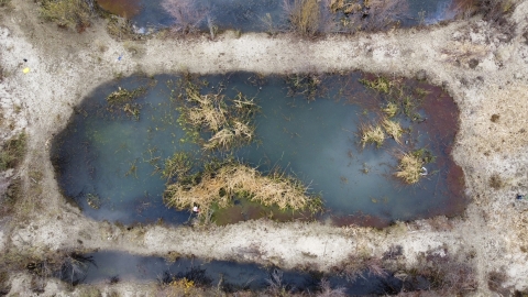 an areal view of a small pound surrounded by dry grass.