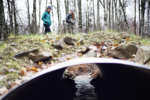 two women walk over a road culvert 