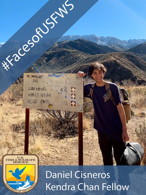 A man standing next to an outdoor sign. A banner reads "#FacesofUSFWS" and another banner reads "Daniel Cisneros Kendra Chan Fellow"