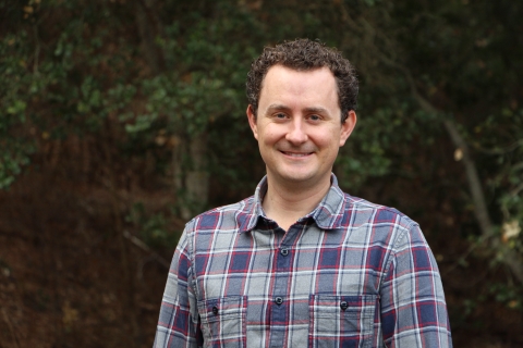 A man wearing a grey, purple, and red checkered shirt