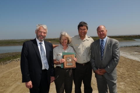 Four smiling people standing side by side. The second person from the left is holding an award.