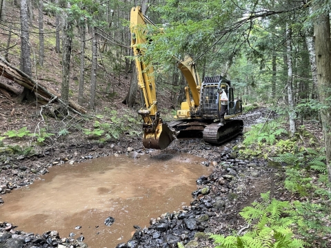 Excavator on stream bed creating pool