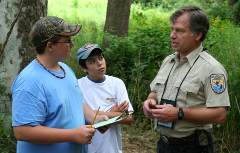 A man in a US Fish & Wildlife Service uniform talking to children in a forest