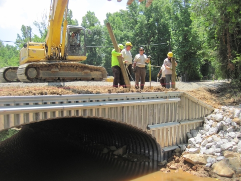 A construction crew stands atop a newly-installed culvert