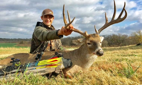 A young hunter sits behind a harvested white-tail deer buck.