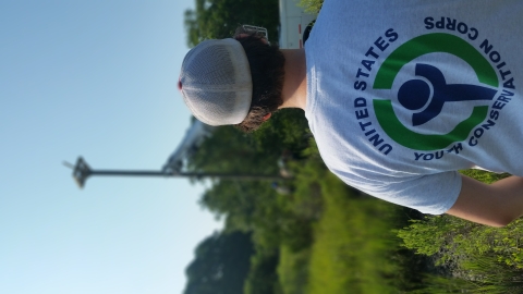 A youth conservation corps boy with his back to the viewer watching as an raptor platform attached to the top of a telephone pole is being anchored into the ground