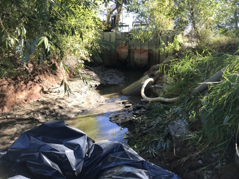 Dewatered stream channel with a pump sucking water out through a large hose.