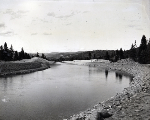 Black and white photo looking down a constructed channel of water.