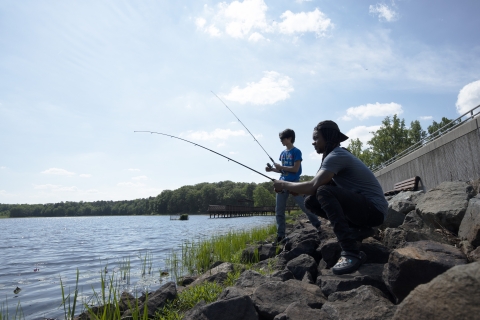 One man and one teen fishing on Cash Lake. They are standing on rocky sore with large white clouds in the sky