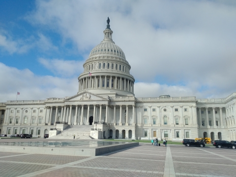 A view of the U.S. Capitol building in the sun with blue sky and clouds in the background