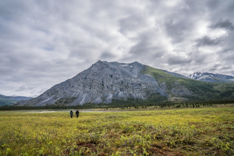 Two small silhoutted hikers on an open tundra with mountains