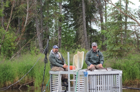 two men sitting atop a metal structure in a river