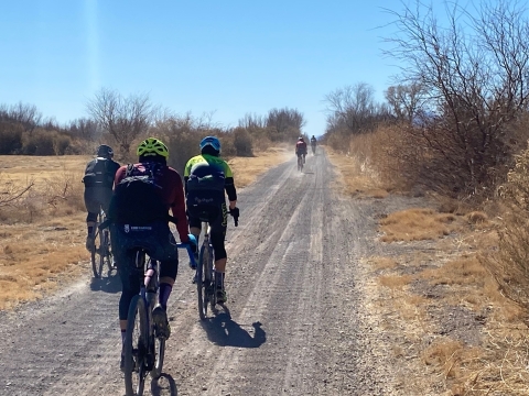 cyclists ride along a dirt road in the desert