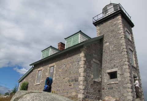 A gray stone lighthouse that looks as much like a regular house as it does a lighthouse