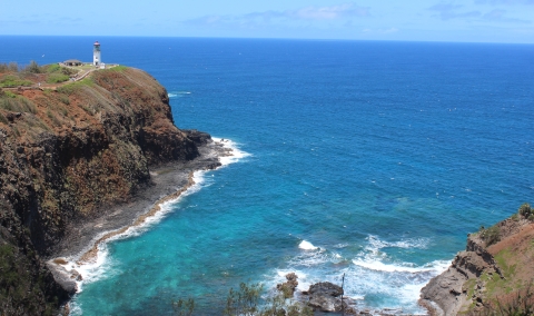 A distant view of a white lighthouse on a rocky bluff overlooking the deep blue ocean