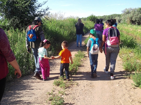 Group of people walking up a grass trail with open sky and high grass on both sides. 