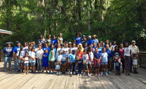 A group of African-American women and children pose for a photo on a boardwalk in front of a forest.