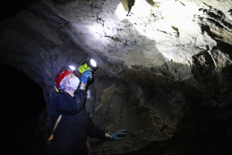 Lone person in an underground passage shines a flashlight on the stone wall.