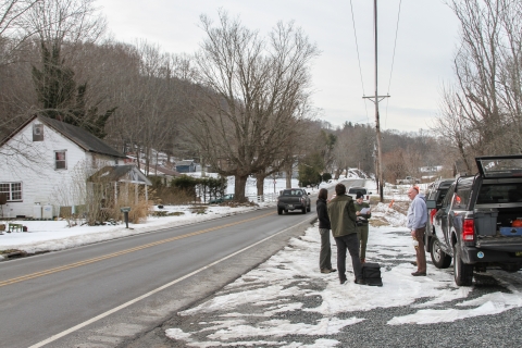 Four people standing between a rural road and a pick-up truck parked on the road shoulder