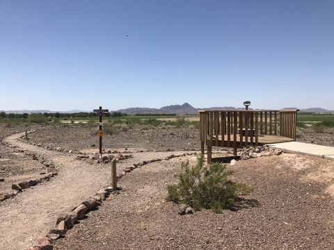 A flat, sunny, rock-lined dirt trail branches off to an observation platform