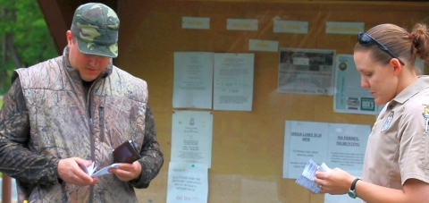 A man in hunting gear and a woman law enforcement officer comparing hunting documents