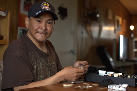 man sits at table with tools, small objects - an ivory carver