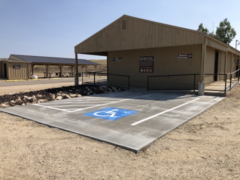 2 long narrow buildings on hard dirt ground. In front of one is parking pad with disabled parking logo in parking spot.