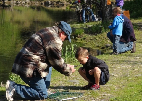 Man kneels down to put a hook on a young boys fishing line. 