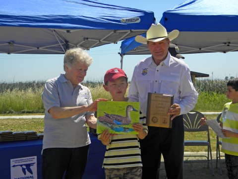 A male child holds his art up while receiving an award