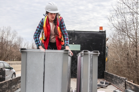 Person standing in the back of a flat-bed truck, examining a large, box-like object